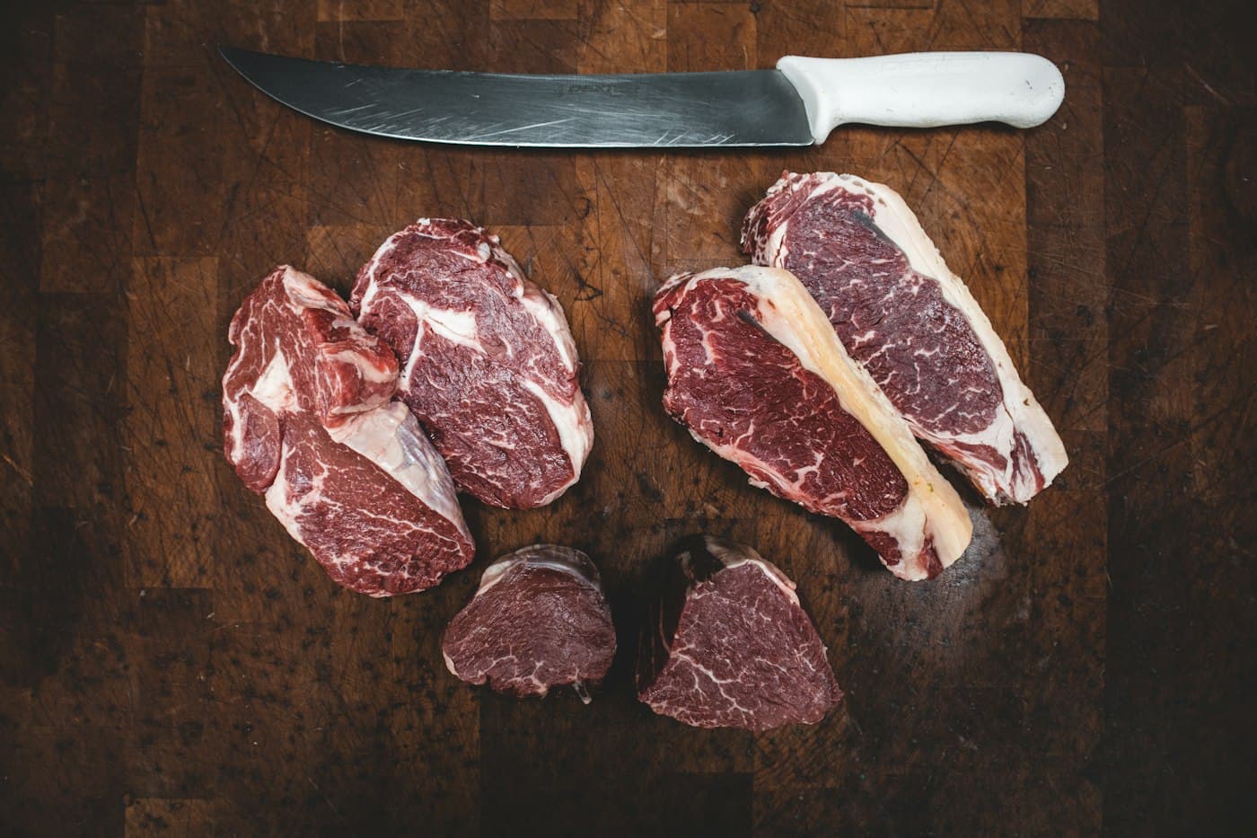 Verschiedene Stücke frisches Rindfleisch mit einem Fleischermesser auf einem dunklen Brett