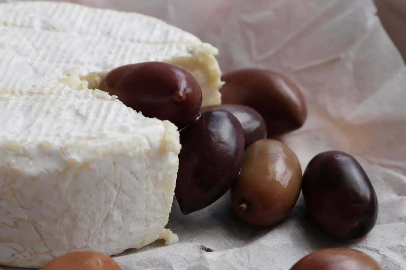 Ein Laib weißer Käse neben dunklen Oliven