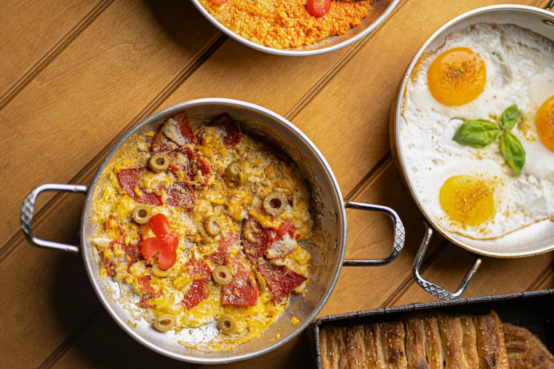 Menemen mit Tomaten, Paprika und Ei in einer Pfanne, daneben Spiegeleier und Tee